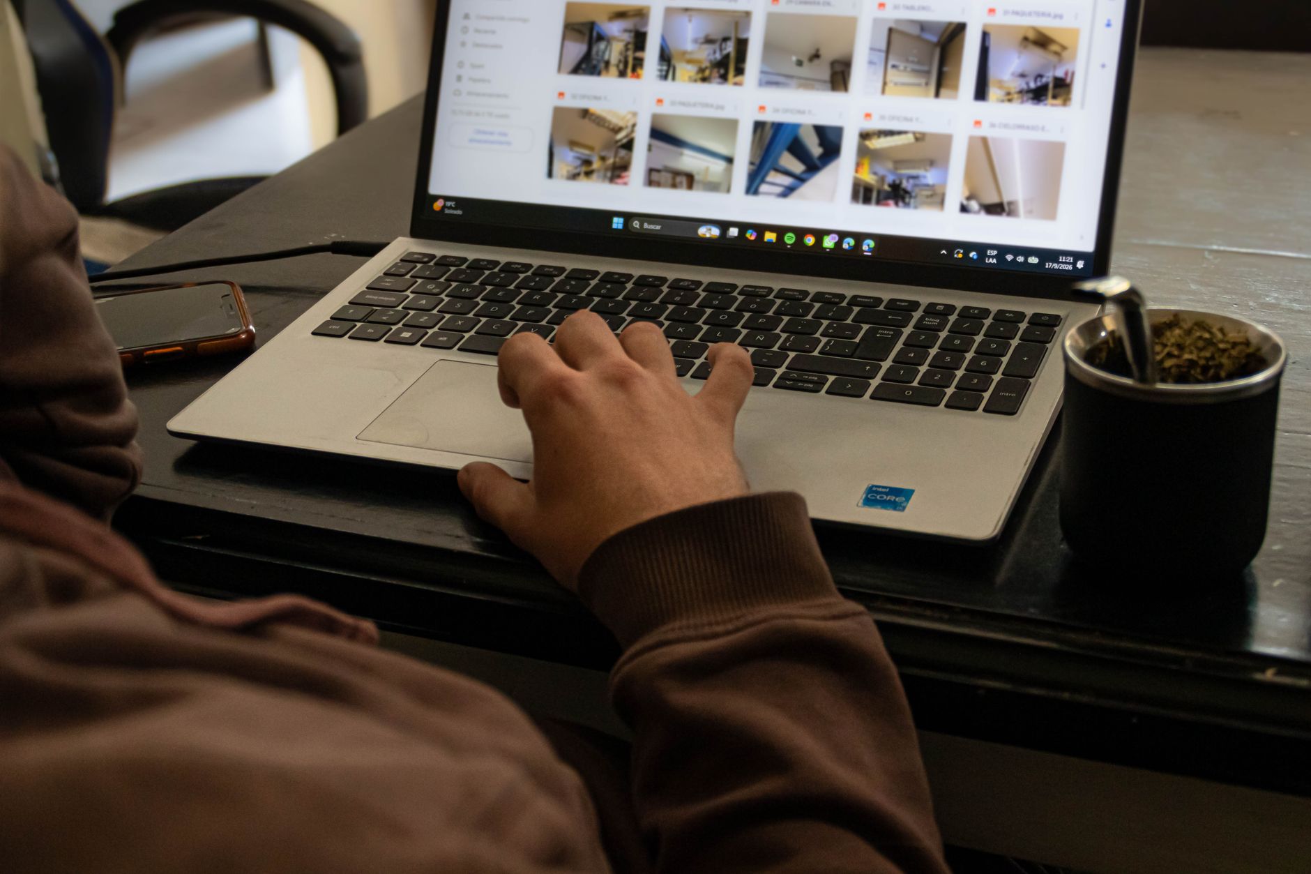 A close-up of a person browsing images on a laptop, with mate drink nearby.
